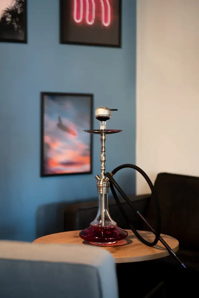 Narguilé à base rouge sur une table ronde devant un mur de cadres