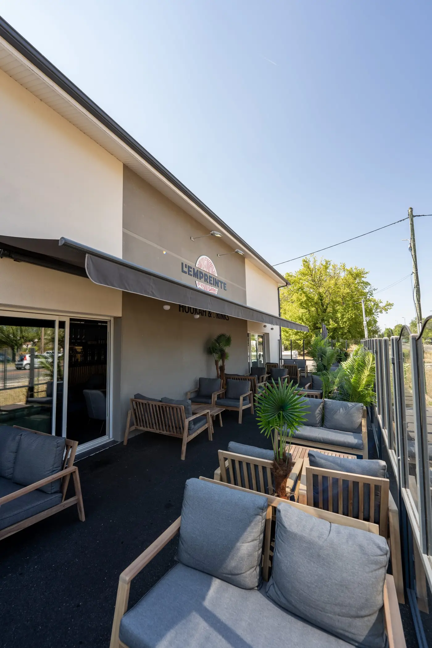 Façade de L'empreinte avec son store et sa terrasse aménagée de bancs et de coussins