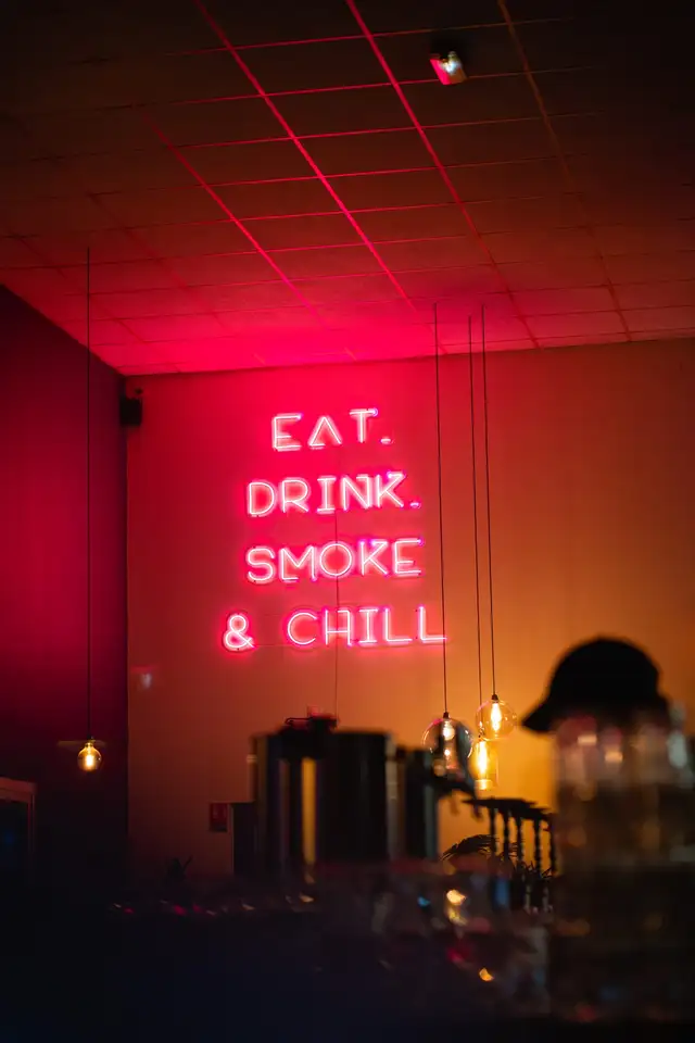 Salle baignée de lumière néon rose avec le comptoir du bar au fond